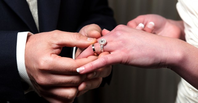 Groom placing wedding ring on brides finger 